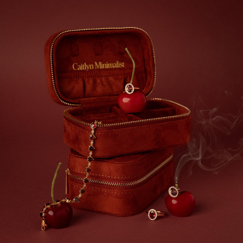 The Cherry Red Velvet Jewelry Case, featuring gold zippers and cherry accents, is shown with a ring, bracelet, and smoke on a red backdrop—ideal for stylish luxury jewelry storage.