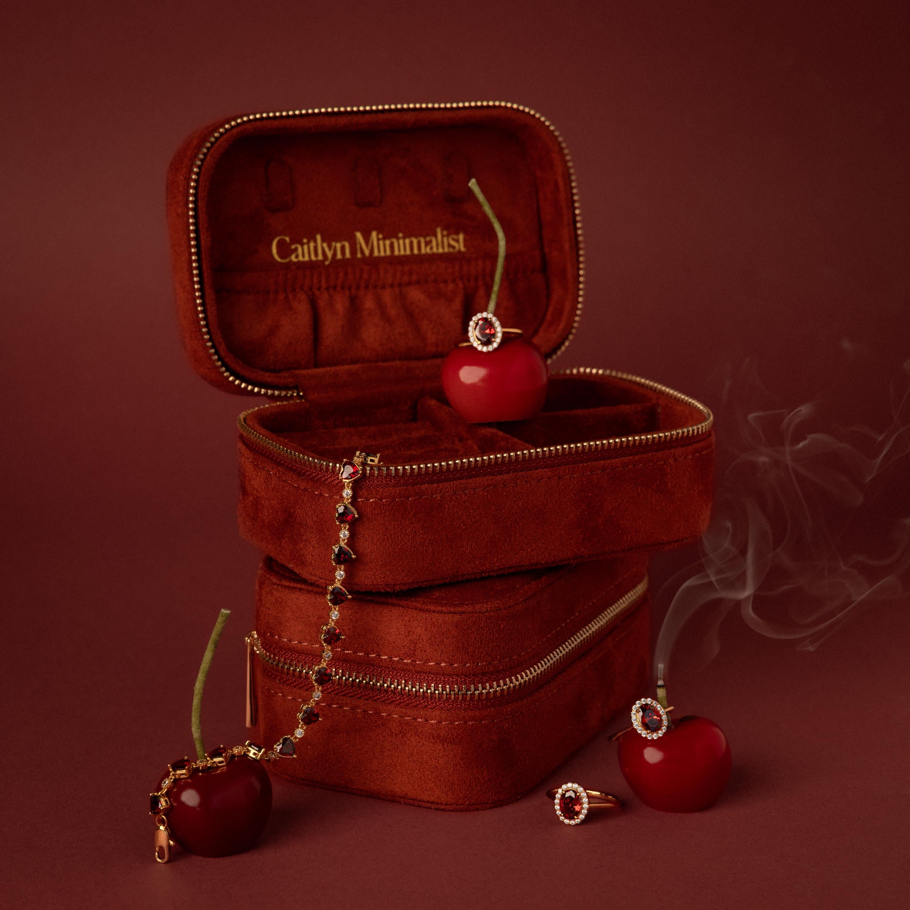 The Cherry Red Velvet Jewelry Case, featuring gold zippers and cherry accents, is shown with a ring, bracelet, and smoke on a red backdrop—ideal for stylish luxury jewelry storage.