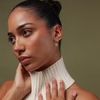 Model showcasing our Pave Bow Charm Hoops styled with diamond studs against a green background