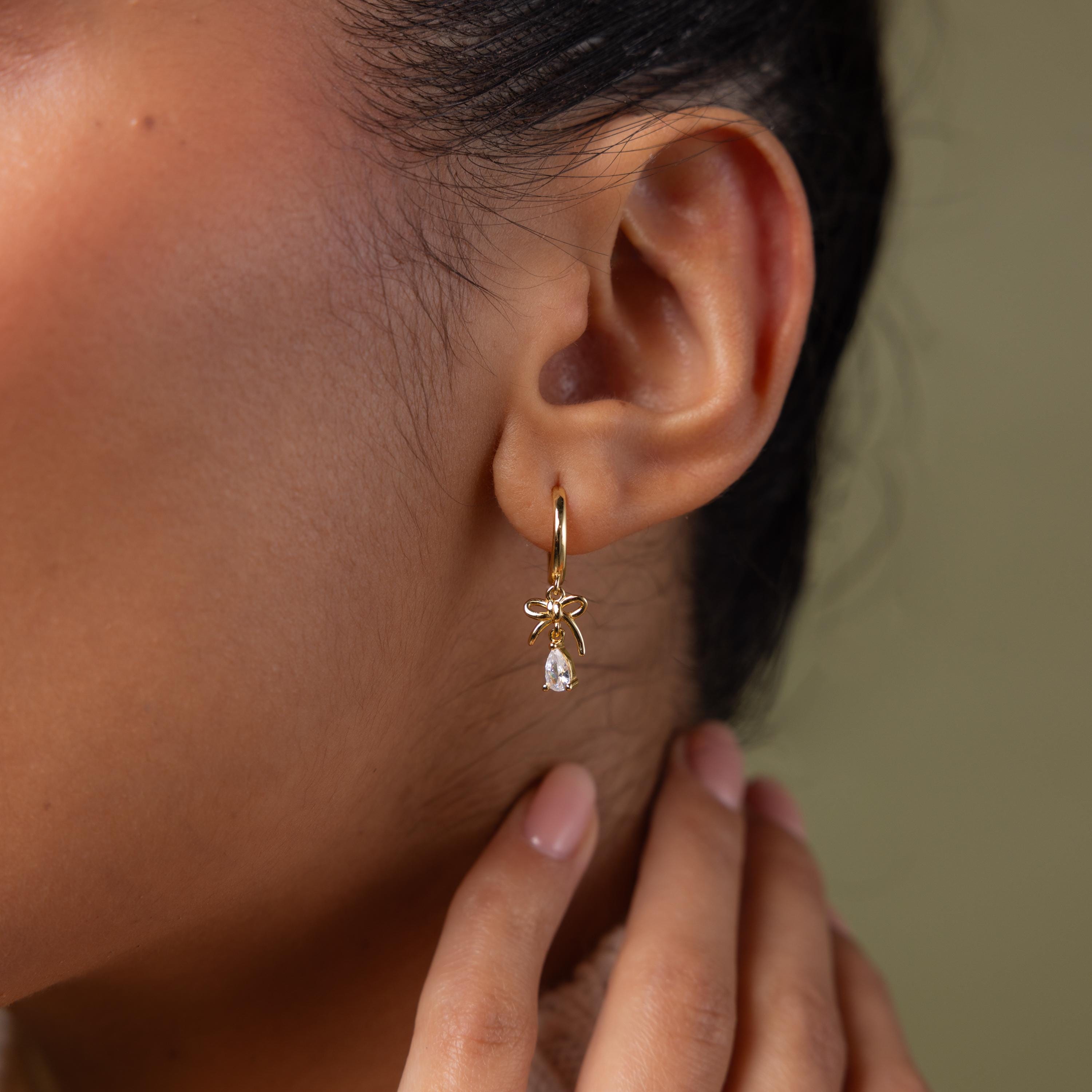 Close-up of a model wearing our Teardrop Ribbon Charm Hoops in gold 