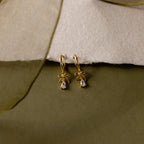 Flatlay of our Teardrop Ribbon Charm Hoops in Gold against a white and green background