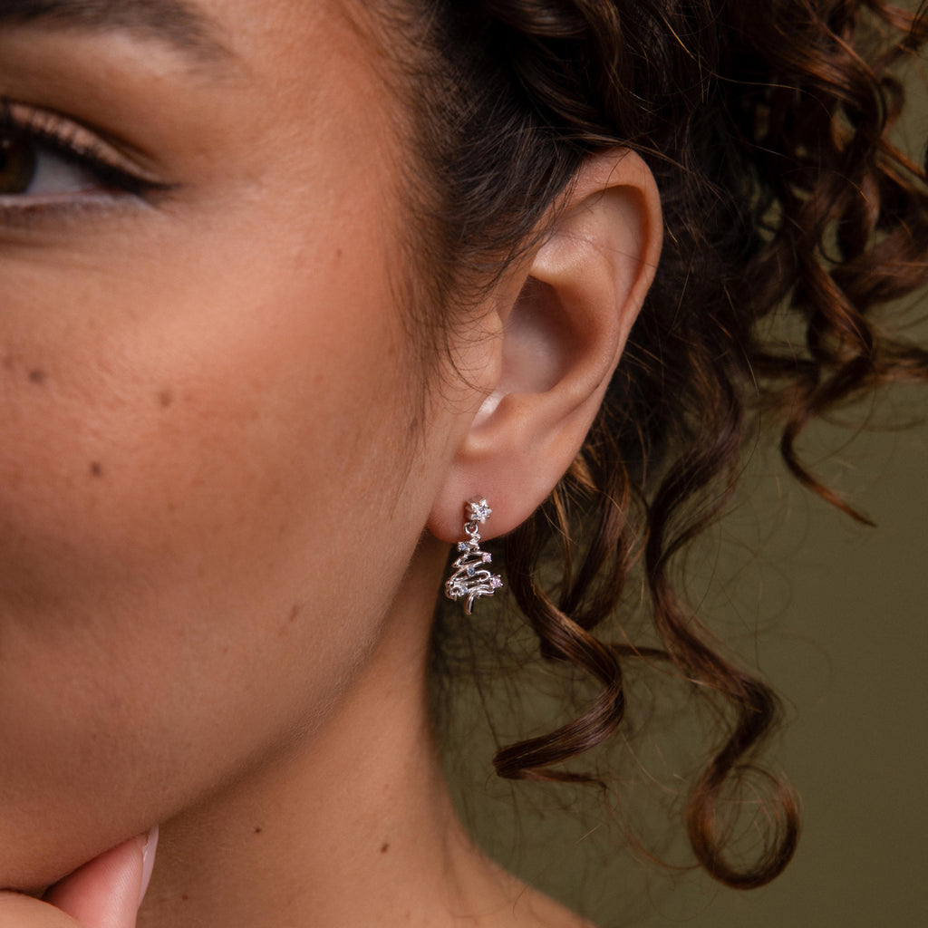 Close-up of a woman wearing our Holiday Tree Studs in silver earring with a green background