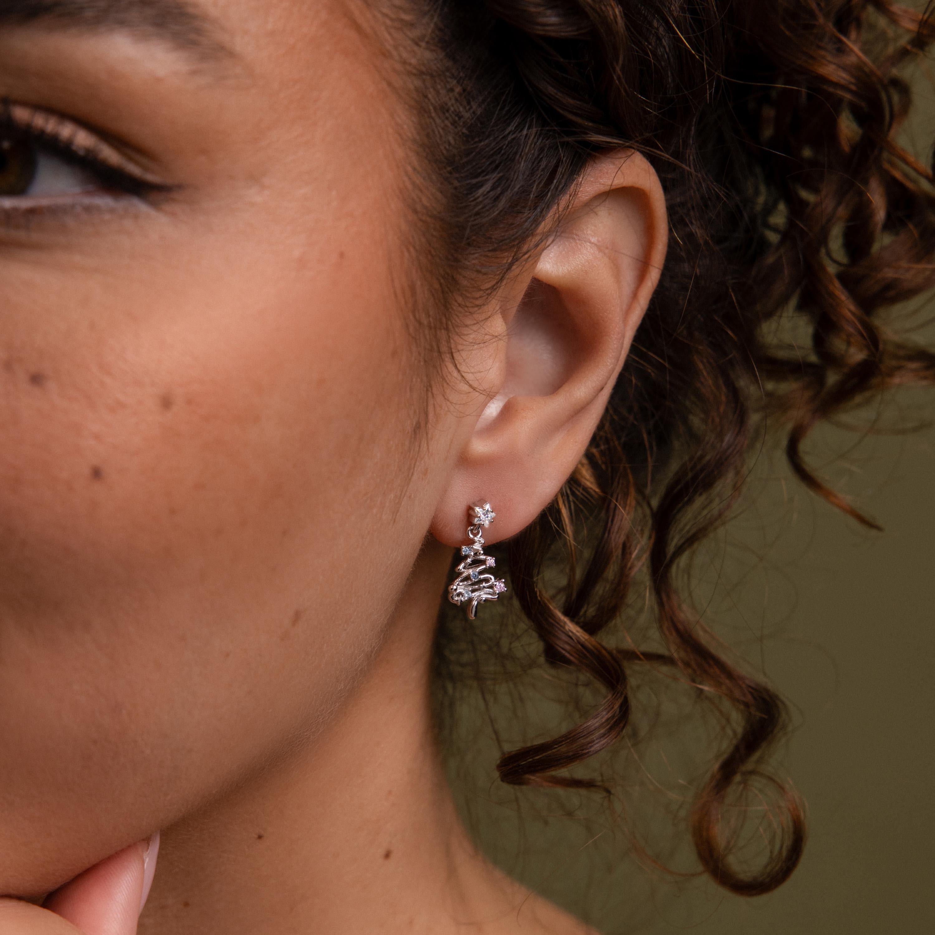 Close-up of a woman wearing our Holiday Tree Studs in silver earring with a green background