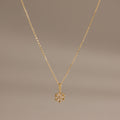 Flatlay of our Diamond Poinsettia Pendant Necklace in Gold on a brown background