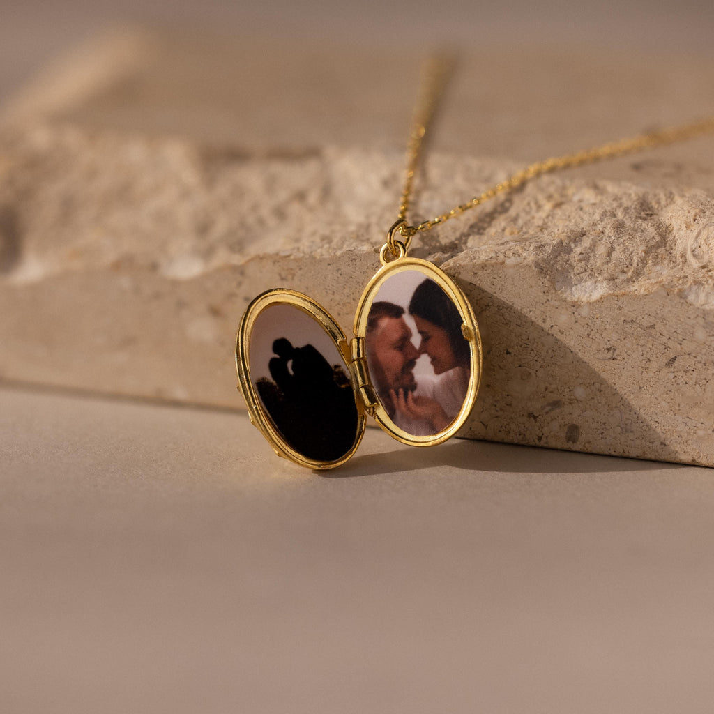The Floral Handwriting Locket Necklace in 18K Gold opens to reveal a photo of a couple embracing, making it a cherished keepsake.
