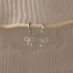 Flatlay of our Pave Bow Charm Hoops
 in Silver on a beige fabric background