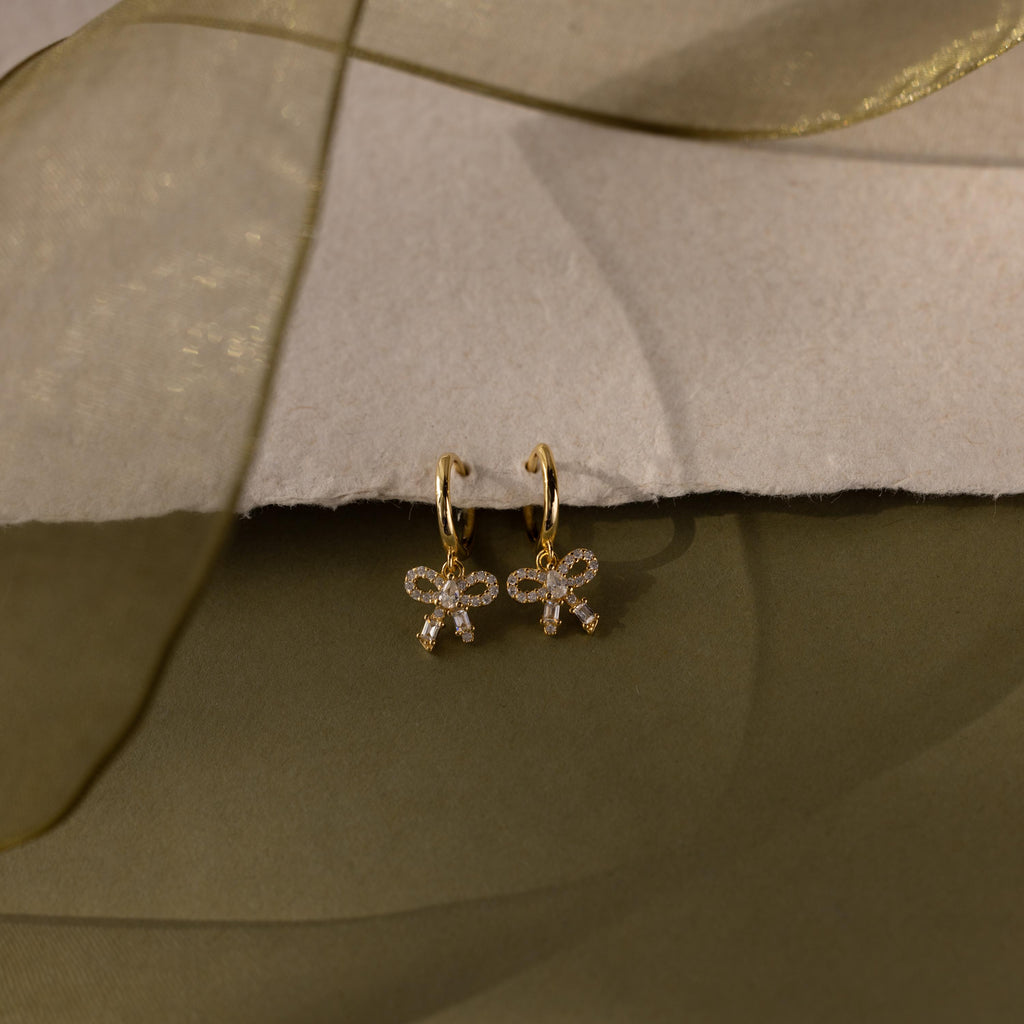 Flatlay of our Pave Bow Charm Hoops earrings on a soft fabric background
