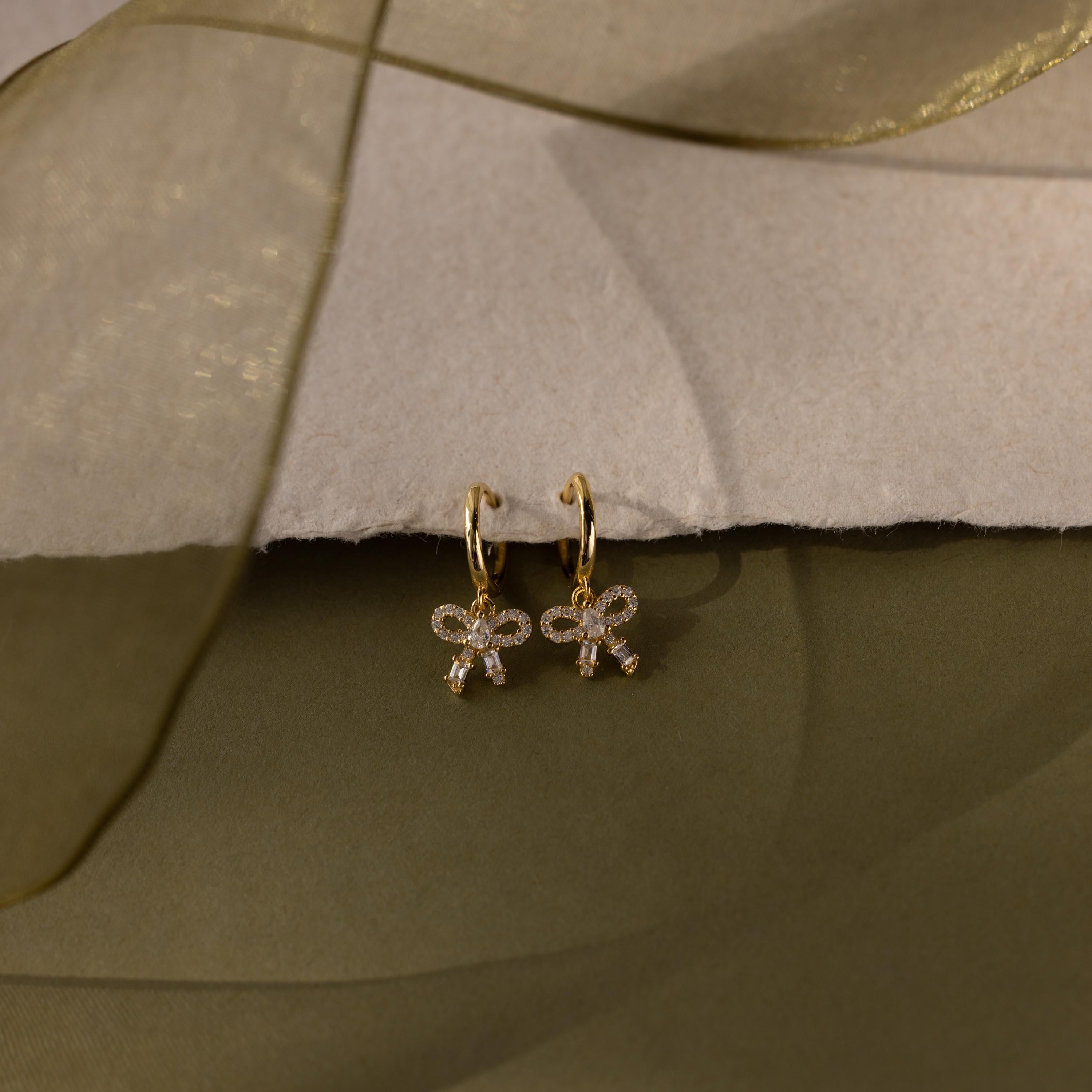 Flatlay of our Pave Bow Charm Hoops earrings on a soft fabric background