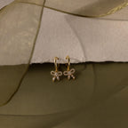 Flatlay of our Pave Bow Charm Hoops earrings in Gold on a soft fabric background