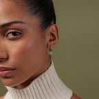 Close-up of a woman wearing our Pave Bow Charm Hoops against a neutral background