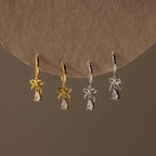 2 pairs of our Teardrop Ribbon Charm Hoops, gold and silver, hanging against a brown background.