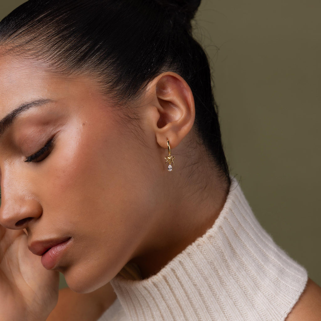 Close-up of a model wearing our Teardrop Ribbon Charm Hoops in Gold