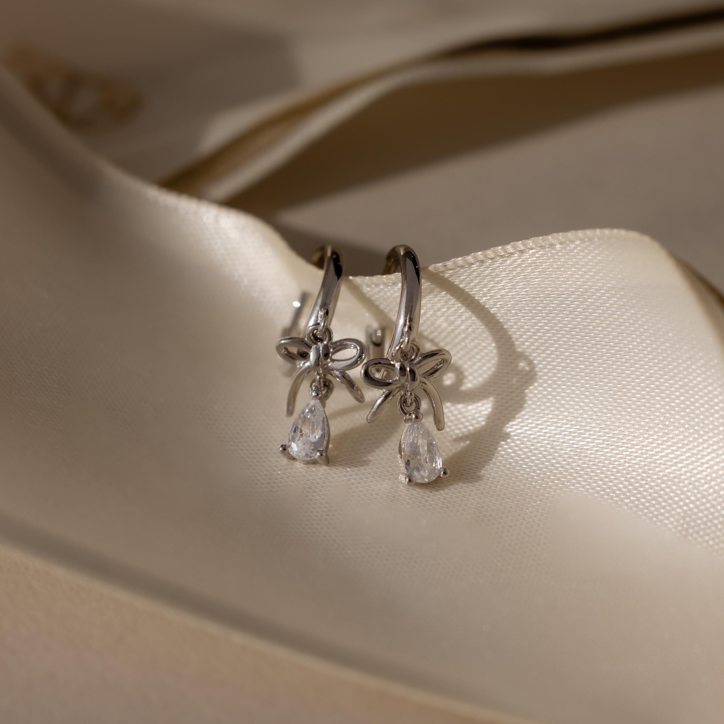 Flatlay of our Teardrop Ribbon Charm Hoops in Silver against a beige ribbon