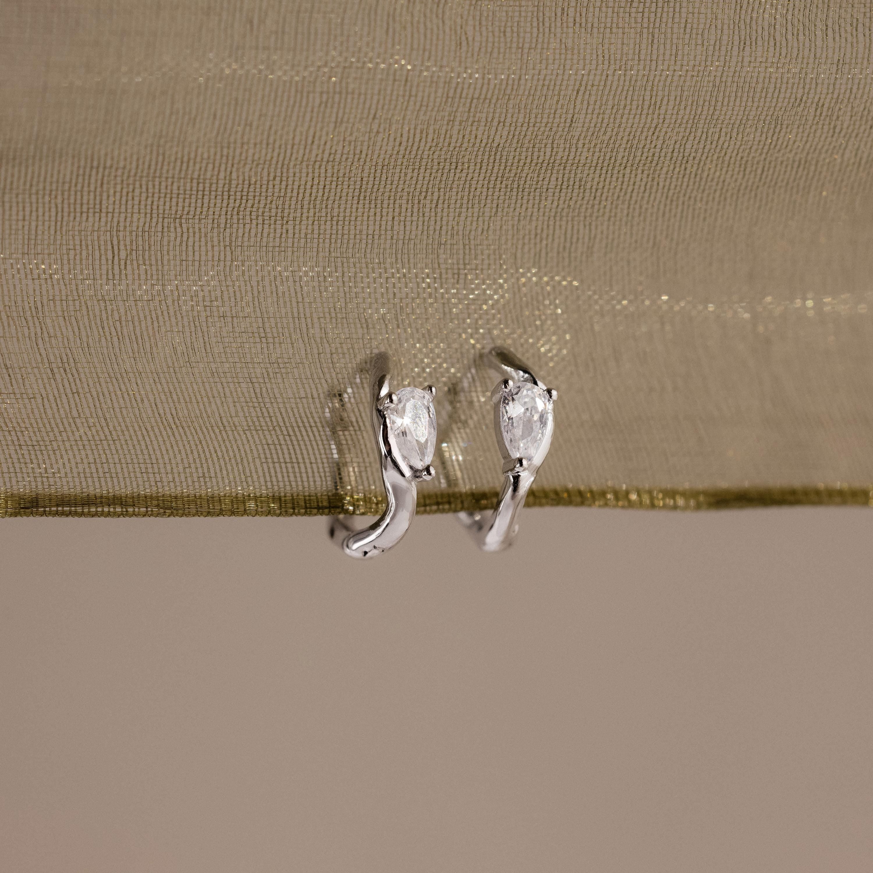 Flatlay of our Hammered Diamond Teardrop Hoops in Silver against a green ribbon
