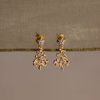 Gold Christmas tree earrings with Pink and Aquamarine gemstones on a beige fabric background