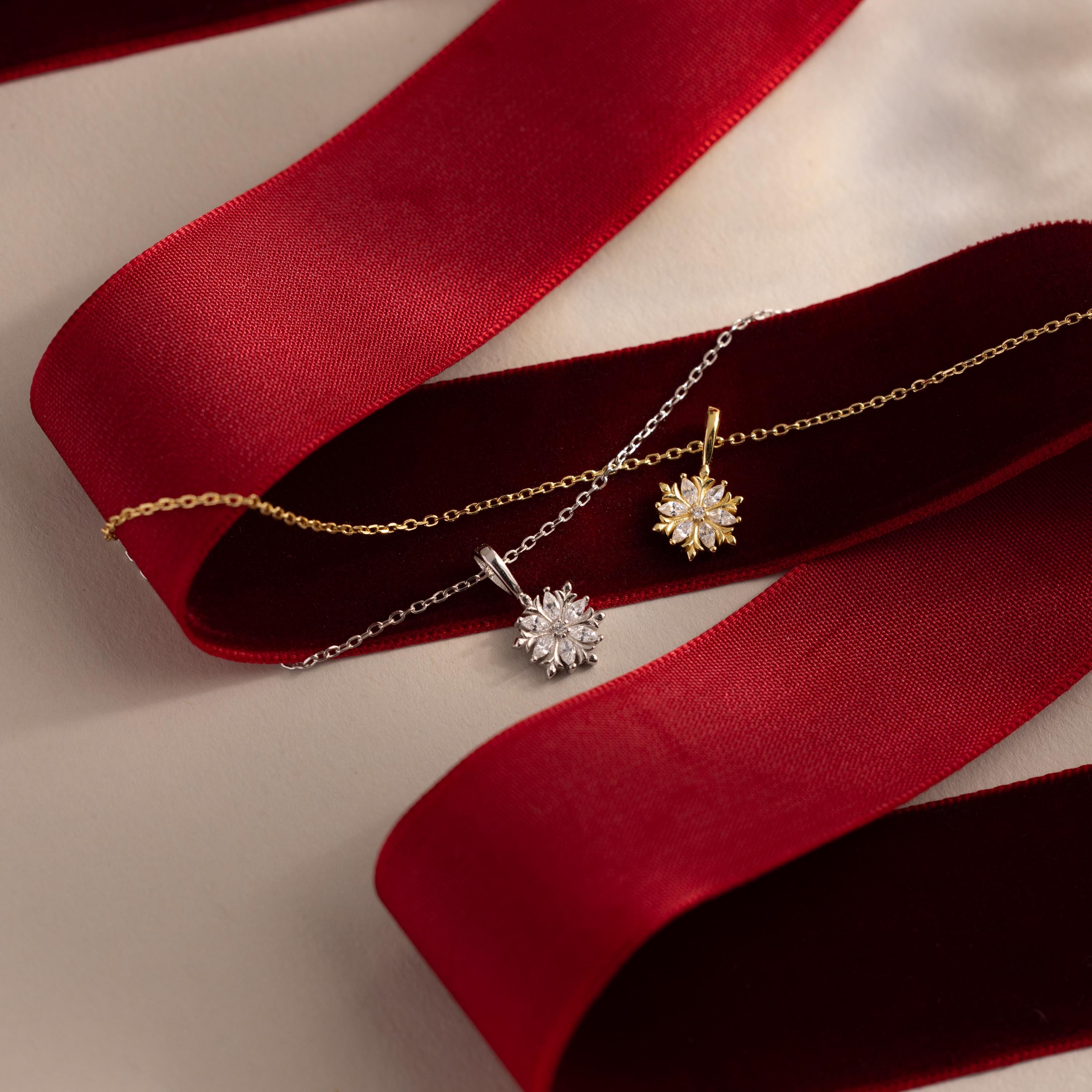 Flatlay of our Diamond Poinsetta Pendant Necklaces in Gold and Silver on a red ribbon