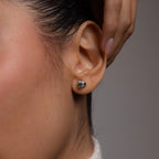 Close-up of an ear wearing a silver earring with a knot design on a neutral background