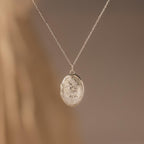 Floral Handwriting Locket Necklace in Sterling Silver with an oval pendant and delicate chain, adorned with floral engravings—an elegant keepsake set against a soft beige background.