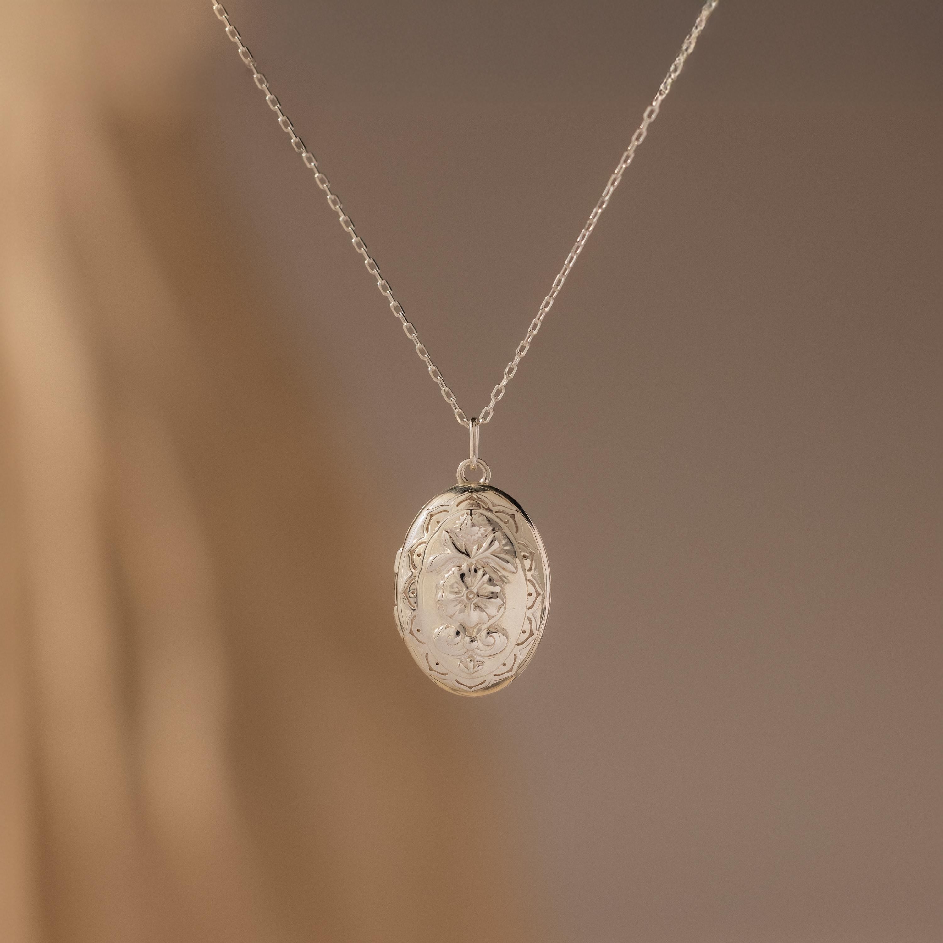 Floral Handwriting Locket Necklace in Sterling Silver with an oval pendant and delicate chain, adorned with floral engravings—an elegant keepsake set against a soft beige background.