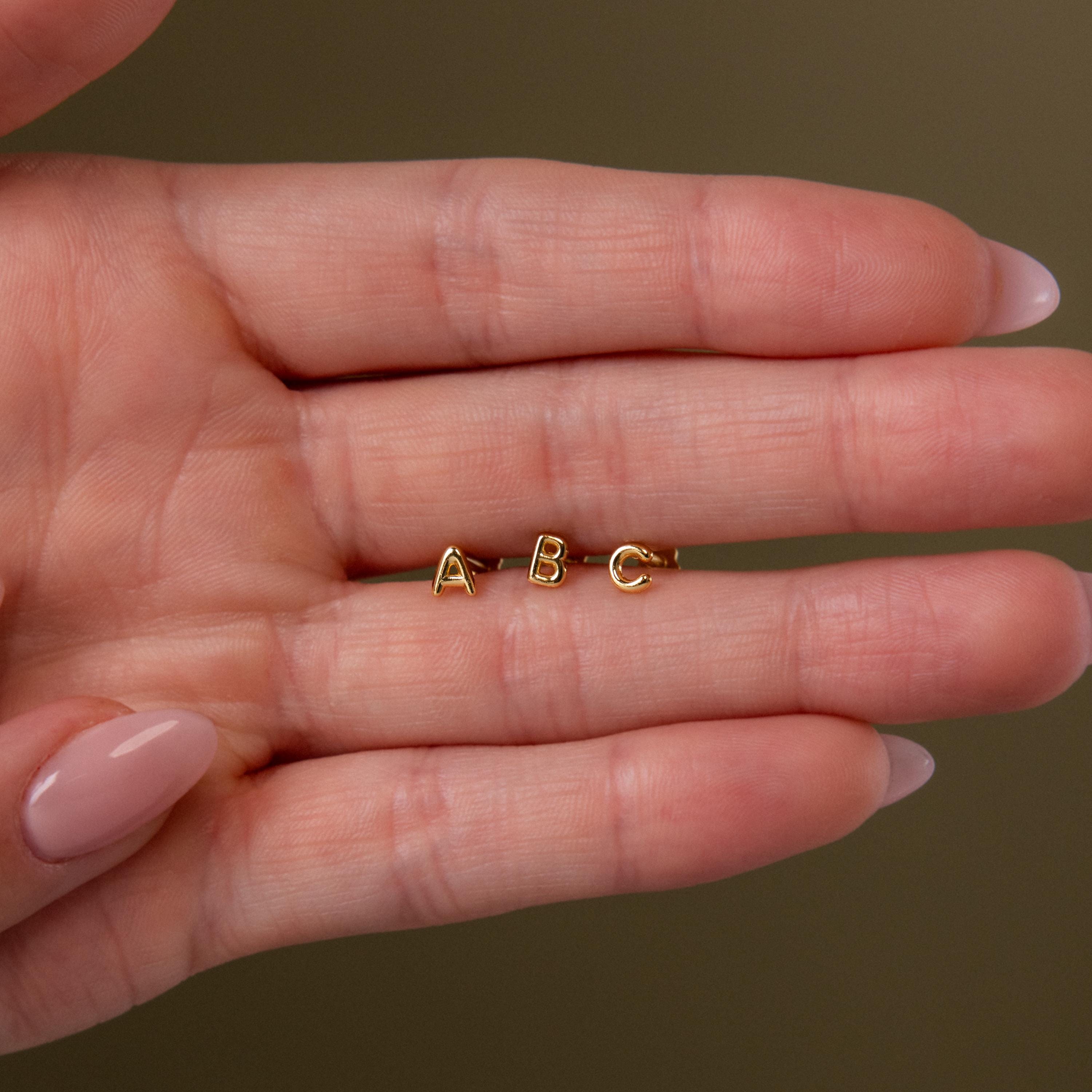Close up of a model's hand holding our Bubble Initial Flatback Studs in between the fingers, showcasing letters A, B & C