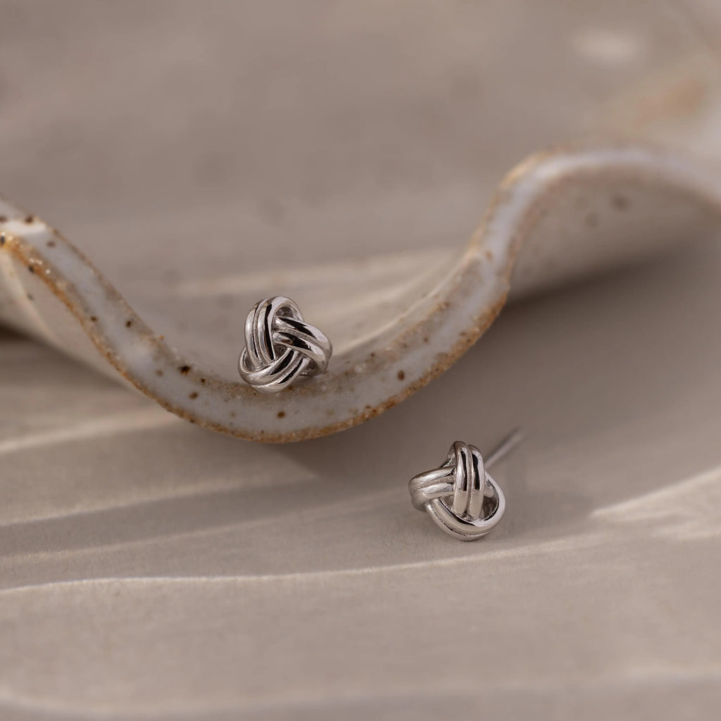Silver knot earrings on a textured beige surface