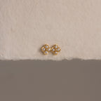 Rounded Pearl Flower Studs featuring a gold bezel, floral design, and white pearls—an elegant choice for bridesmaid jewelry—displayed on a textured off-white surface.