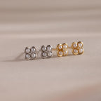 The Rounded Pearl Flower Studs, featuring pearl and crystal accents in gold and silver floral shapes, make an elegant bridesmaid jewelry choice, beautifully displayed on a beige surface.