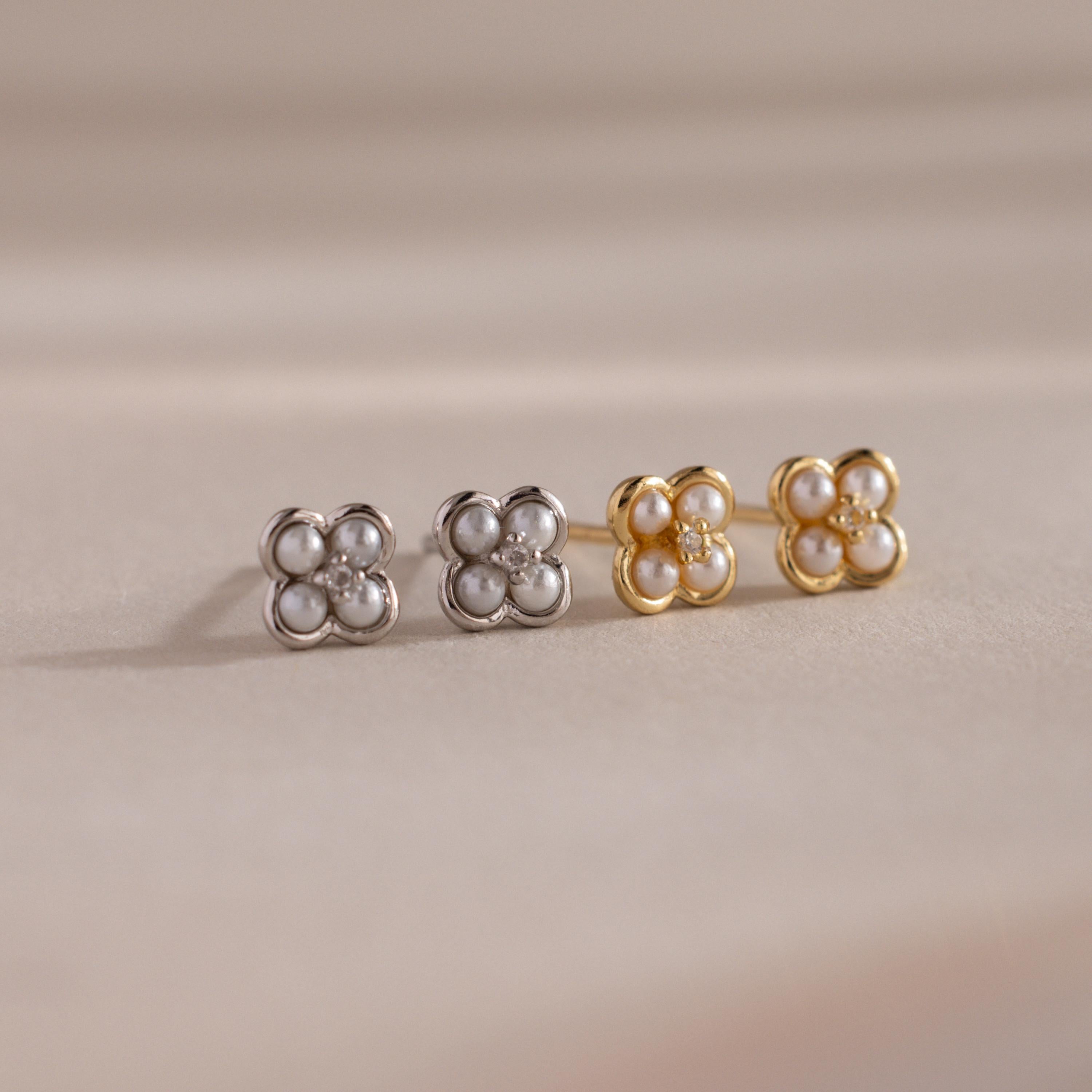The Rounded Pearl Flower Studs, featuring pearl and crystal accents in gold and silver floral shapes, make an elegant bridesmaid jewelry choice, beautifully displayed on a beige surface.