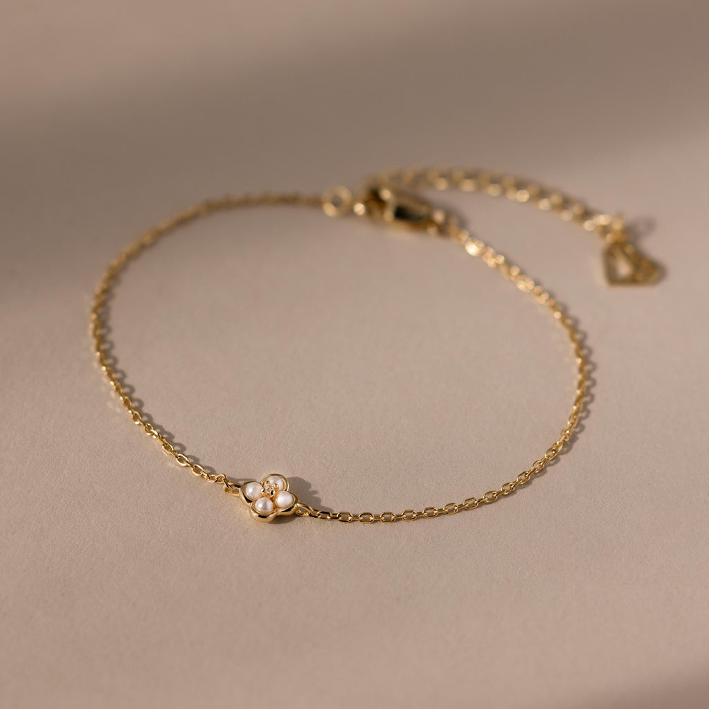 The Rounded Pearl Flower Bracelet features a delicate gold chain with a petite pearl flower charm, making it an elegant choice for everyday wear and perfect for fans of subtle, refined jewelry.