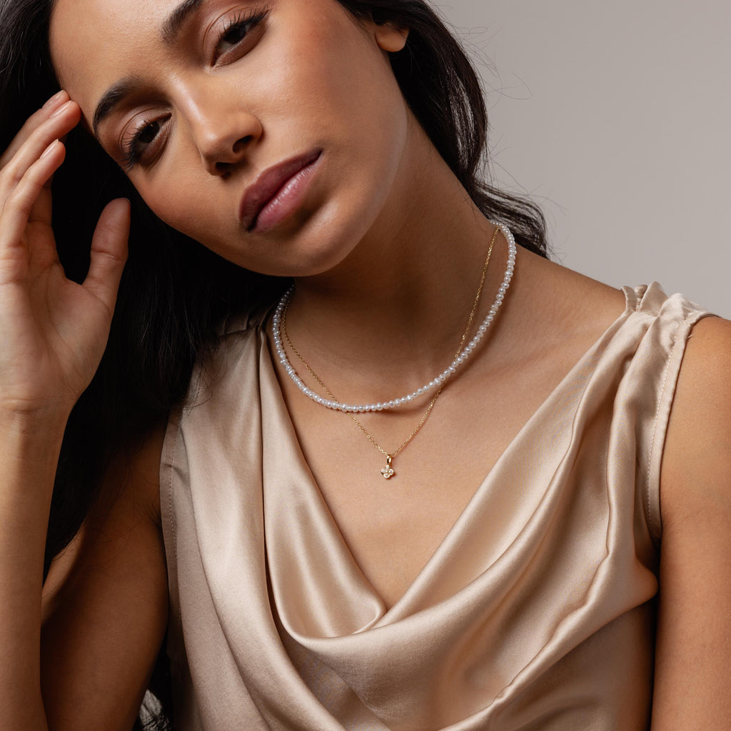 Woman in a satin beige top wearing the Rounded Pearl Flower Necklace, posing with her hand near her face.