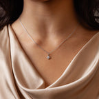 A woman wears the Rounded Pearl Flower Necklace in Sterling Silver, featuring a delicate floral pendant on a silver chain, paired with a beige satin top—perfect for everyday layering.