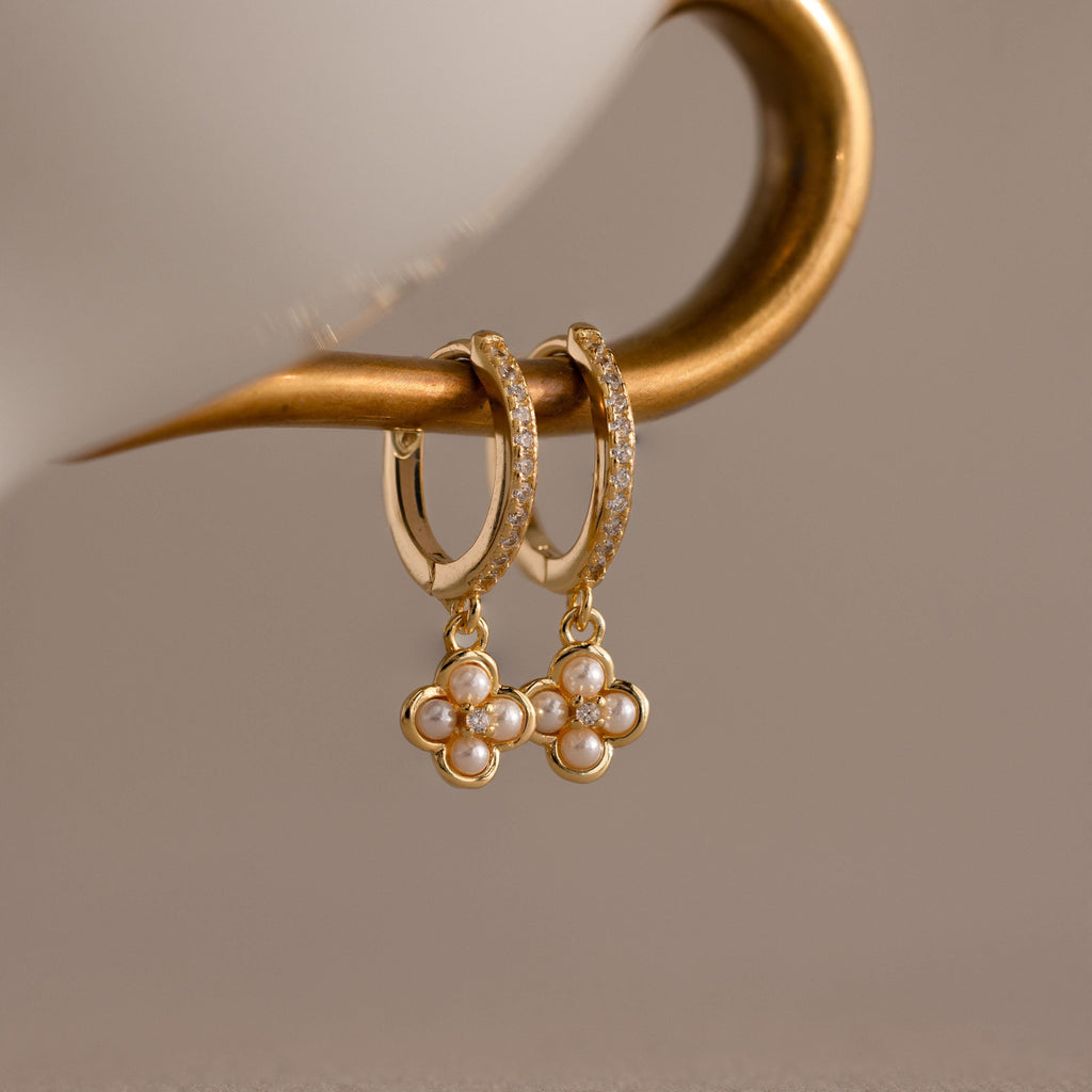Pave Rounded Pearl Flower Hoops—gold hoops featuring pearl and diamond flower pendants, displayed on a curved metallic holder. Elegant wedding earrings ideal for adding romantic charm to any outfit.