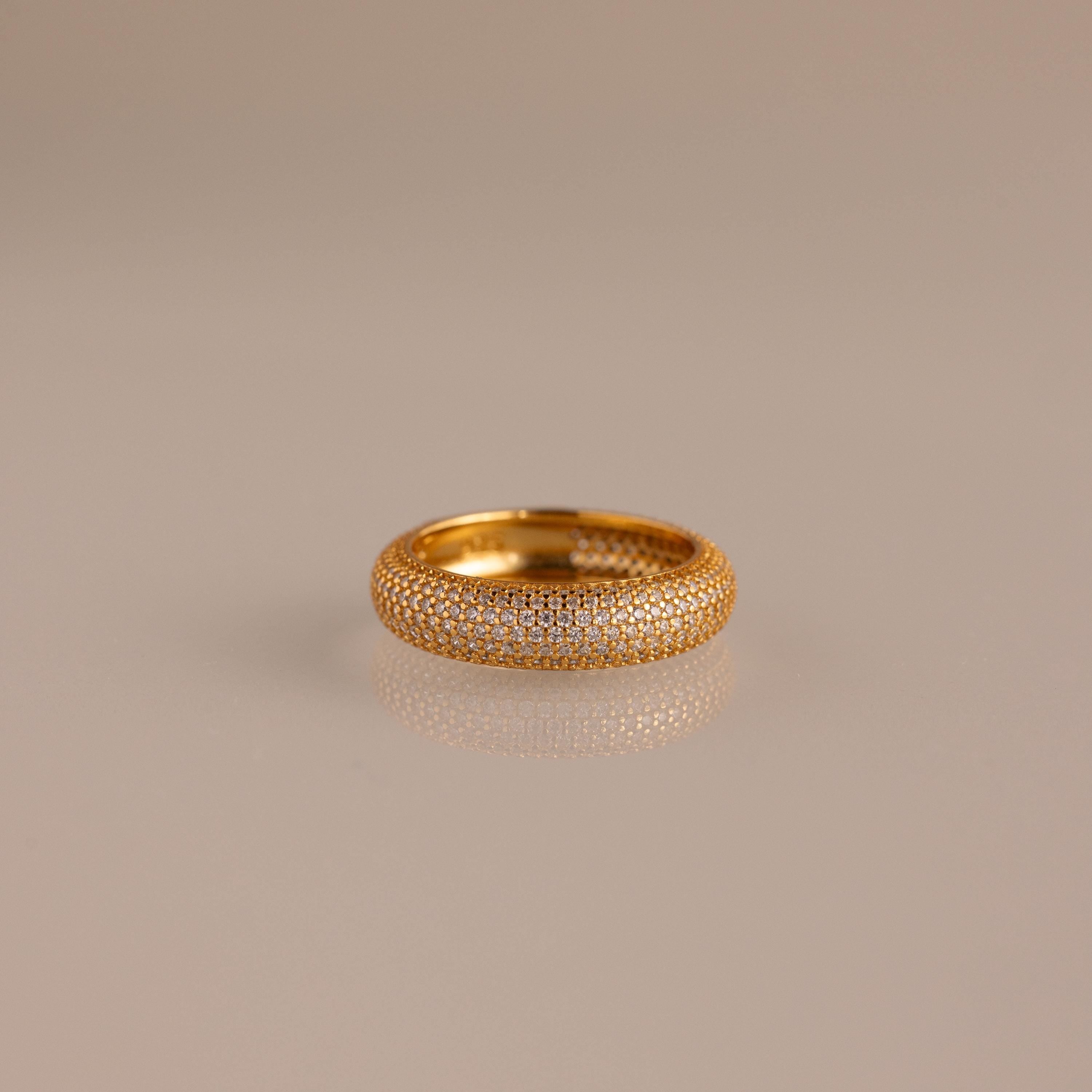 The Bold Pave Stacking Ring, encrusted with small diamonds, gleams on a reflective beige surface.