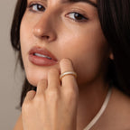 A woman with long dark hair touches her face, showing off the Bold Pave Stacking Ring and a gold textured wedding band on her finger.