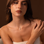 A woman in a white top gazes to the side against a brown background, beautifully showcasing the Diamond Halo Pearl Necklace in Sterling Silver—a stunning piece of timeless jewelry.