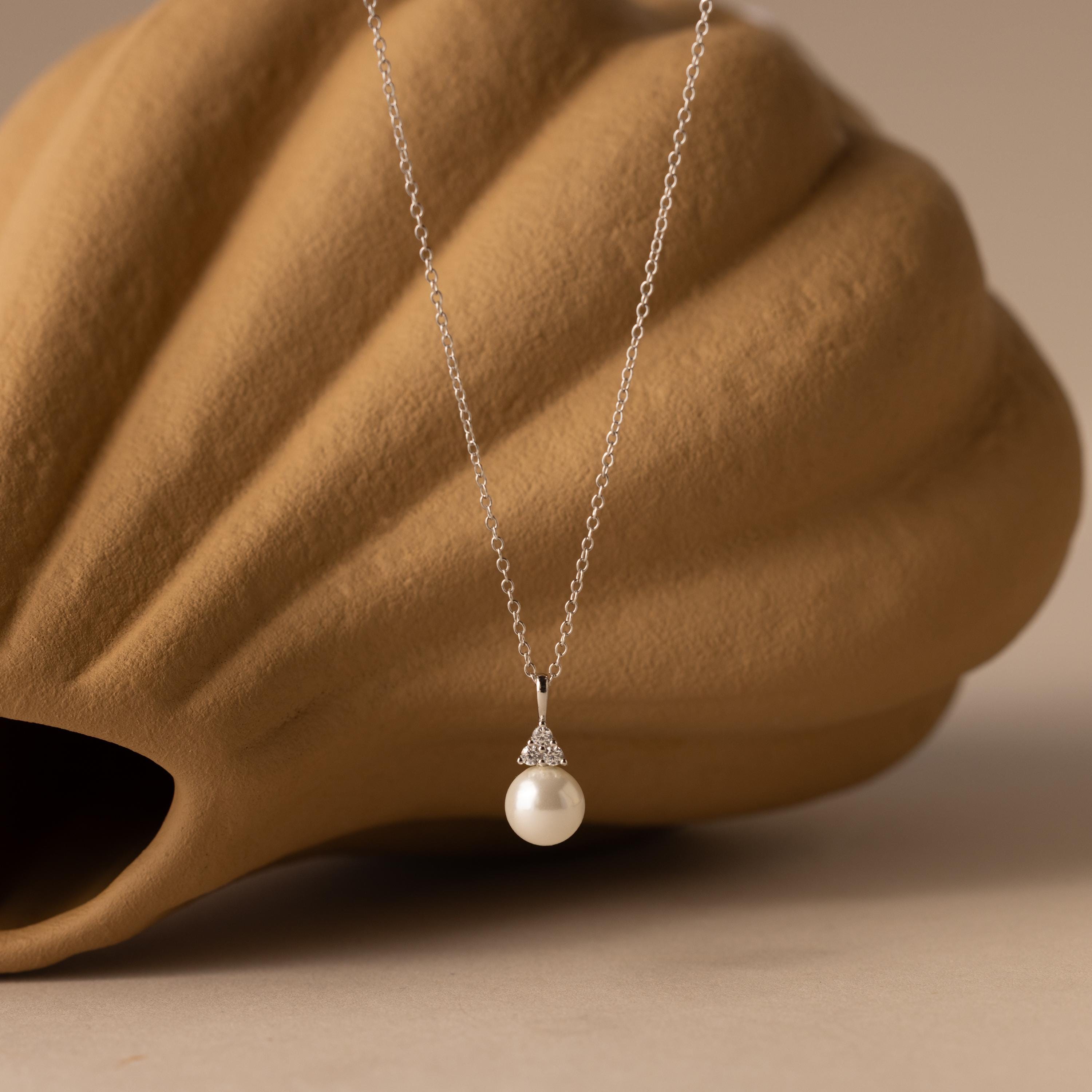 The Diamond Halo Pearl Necklace is elegantly showcased in front of a brown seashell, emphasizing the timeless beauty and sophistication of this stunning jewelry piece.