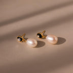 The Midnight Pearl Drop Earrings in 18K Gold showcase oval black accents and large white pearls for an elegant, timeless jewelry statement.