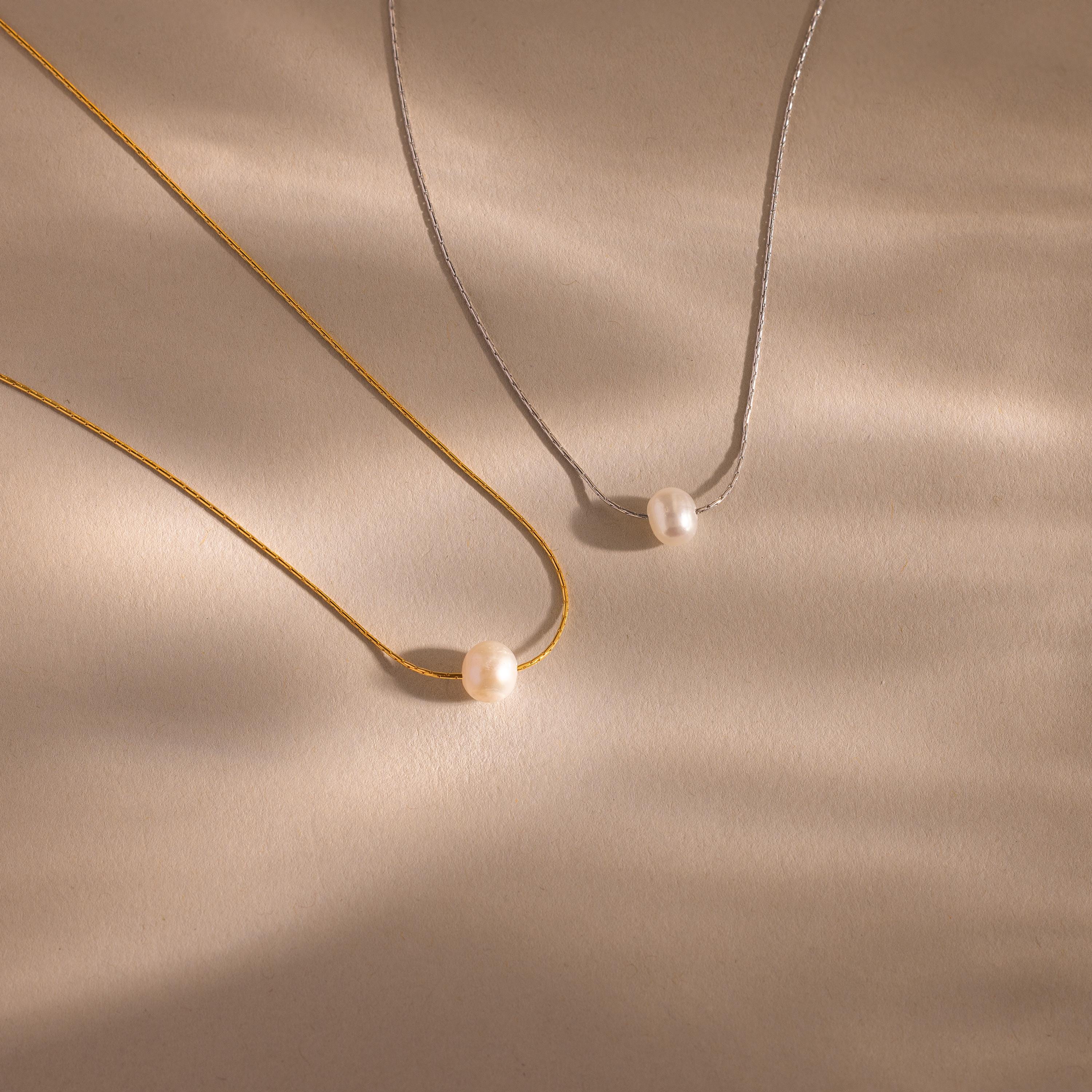 Two Tiny Pearl Dot Necklaces—one gold, one silver—each feature a simple pearl pendant and are displayed on a beige surface with soft shadows.