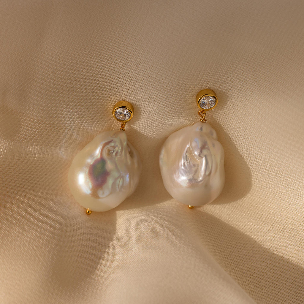 Diamond Baroque Pearl Studs in 18K Gold featuring large baroque pearls and sparkling diamonds are showcased on cream-colored fabric.