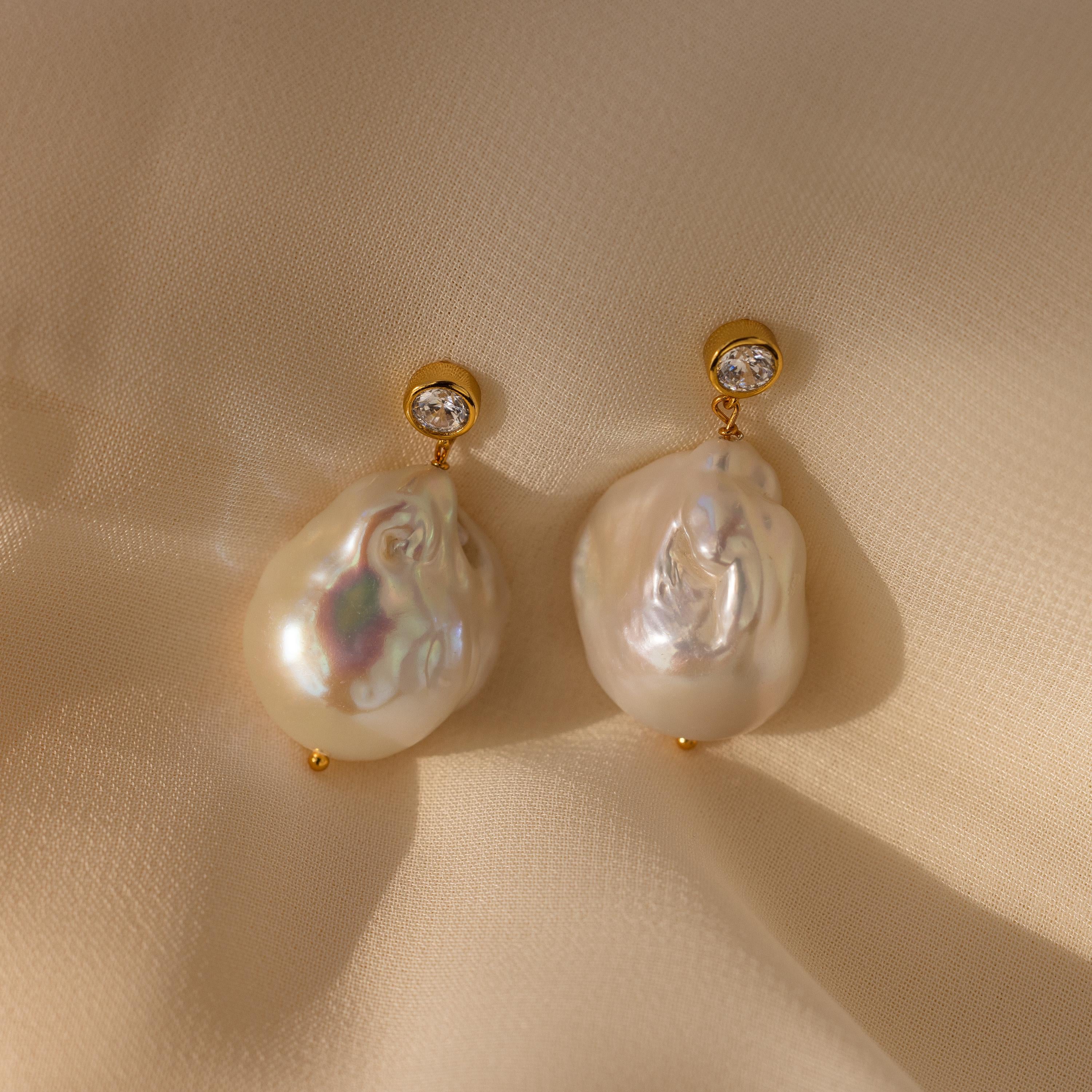 Diamond Baroque Pearl Studs in 18K Gold featuring large baroque pearls and sparkling diamonds are showcased on cream-colored fabric.