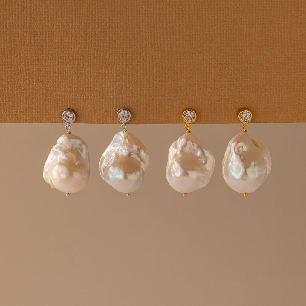 Four Diamond Baroque Pearl Studs—two with silver round posts and two with gold—are displayed on a beige surface, highlighting the organic beauty and elegance of these unique earrings.