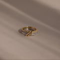 The Pave Mixed Metal Linked Ring Set, featuring gold and silver tones with diamond accents, rests on a smooth beige surface with soft shadows—a versatile piece for any occasion.