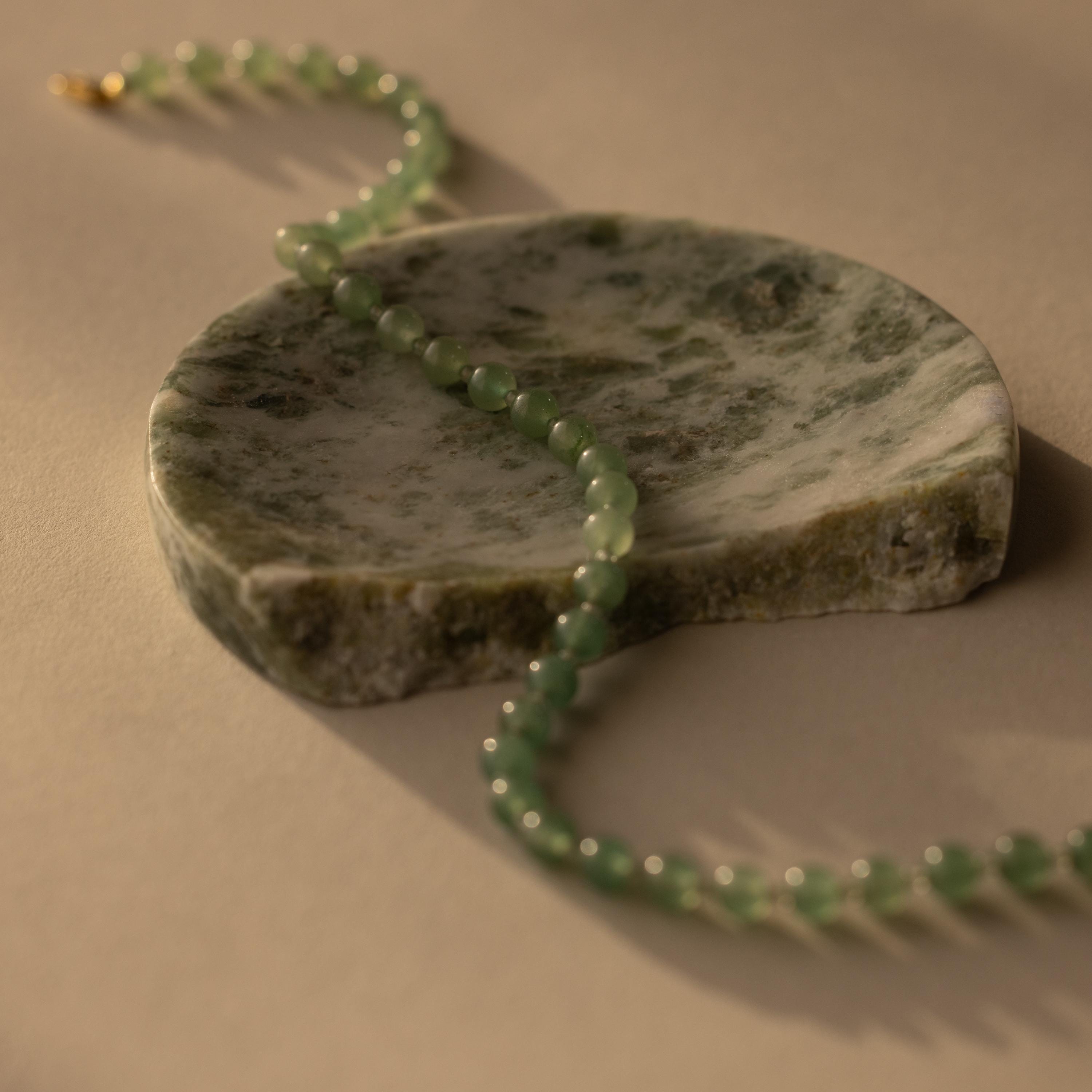 A Jade Choker Necklace is elegantly displayed on a round, green-and-white marble slab set atop a beige surface.