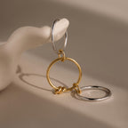 The Mixed Metal Linked Ring Set, featuring intertwined gold and silver hoops, is displayed on a smooth white sculptural hand.
