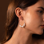 A woman wears Statement Pearl Hoops in Sterling Silver featuring three white pearls, shown in side profile against a brown background—an elegant touch of luxury jewelry.