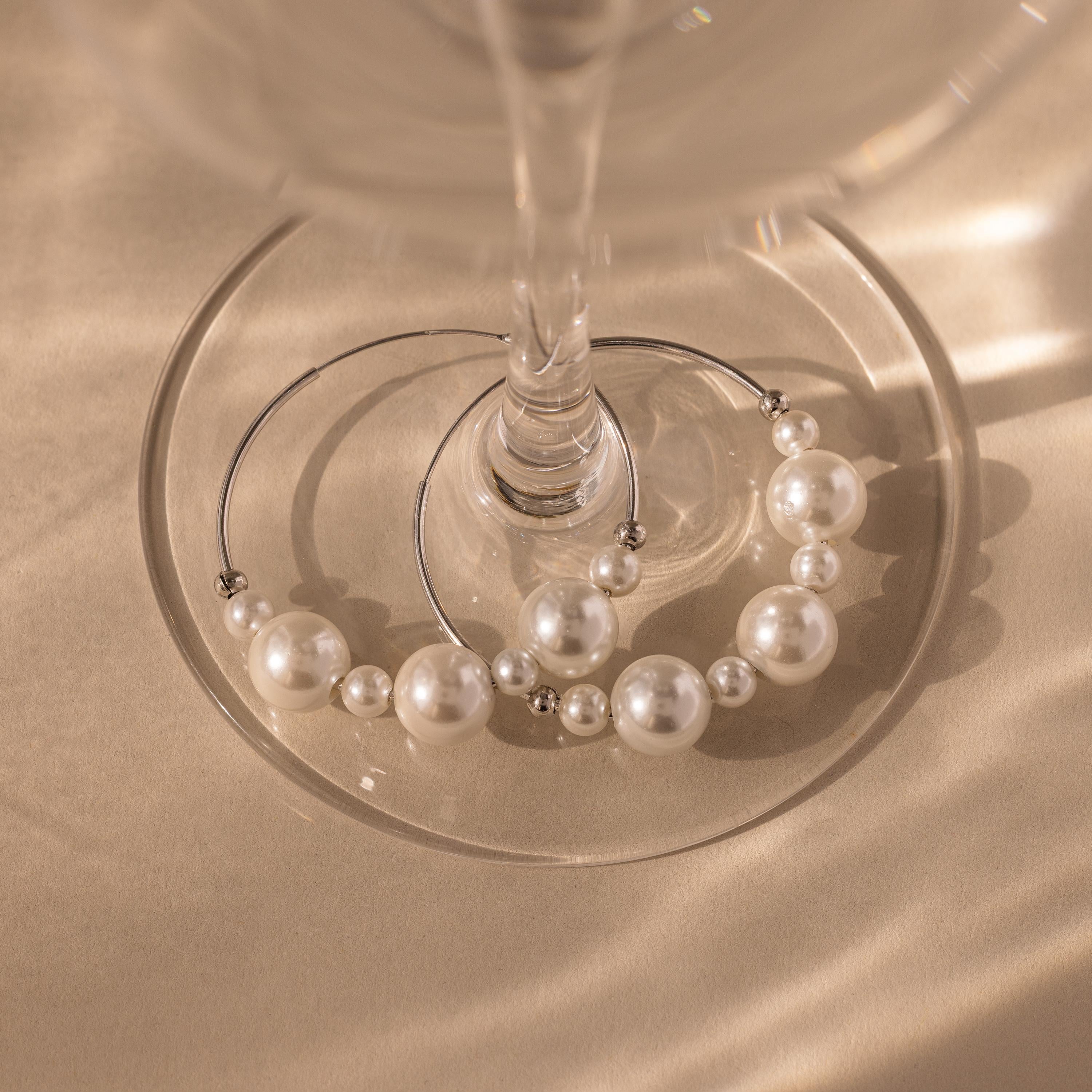Statement Pearl Hoops in Sterling Silver rest at the base of an empty wine glass on a beige surface, bathed in soft light, evoking the timeless allure of luxury jewelry.