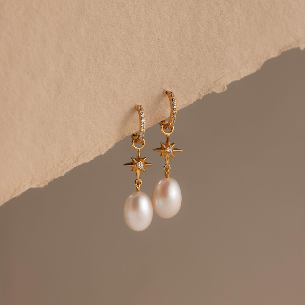 North Star Pearl Hoops featuring elegant pearl drops and star details, showcased on a textured beige surface.