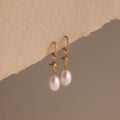 North Star Pearl Hoops featuring elegant pearl drops and star details, showcased on a textured beige surface.