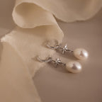 North Star Pearl Hoops adorned with star accents and delicate pearls, showcased on a soft beige fabric background.