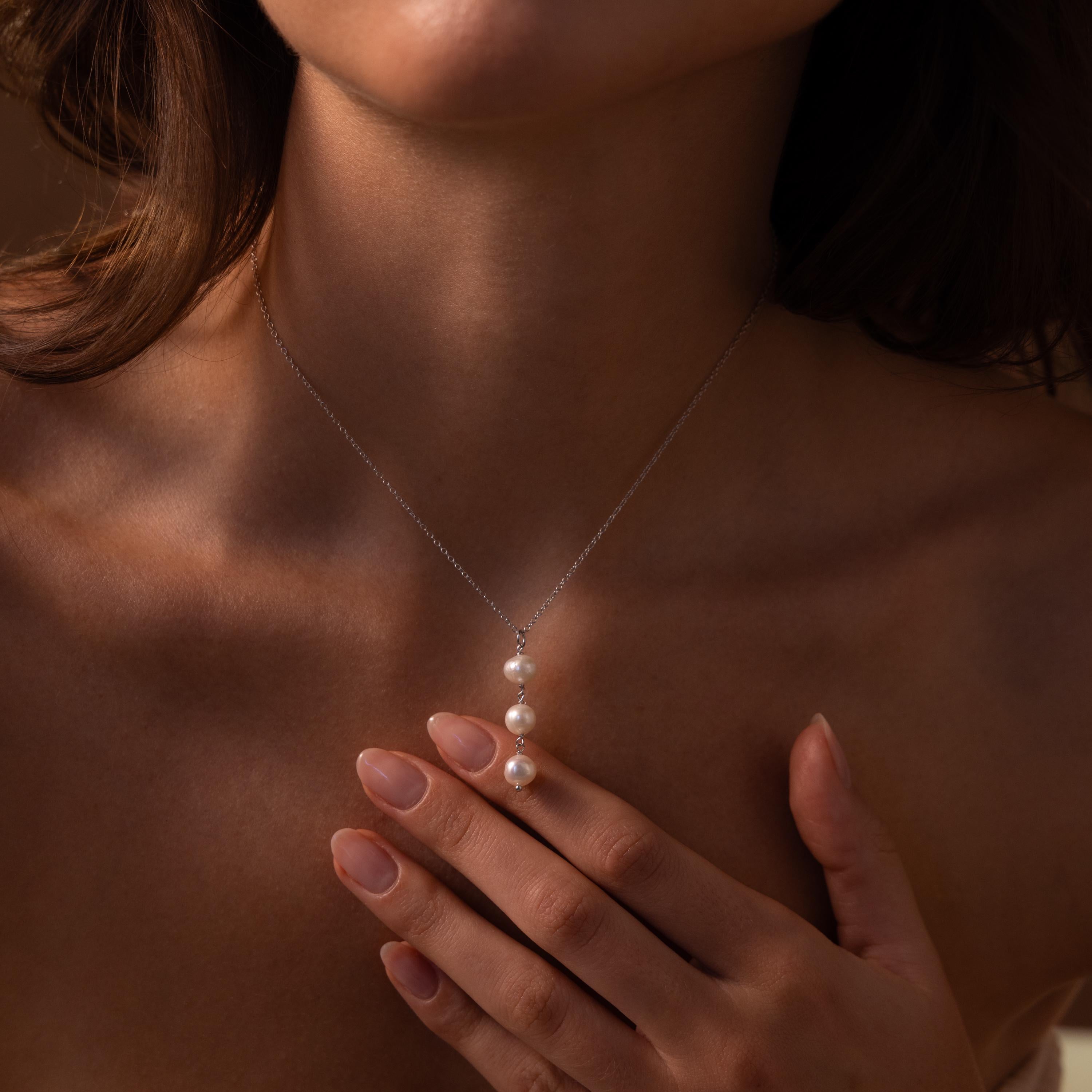 A woman elegantly wears the Pearl Cascade Necklace, featuring three luminous pearls, her hand gently touching the pendant.